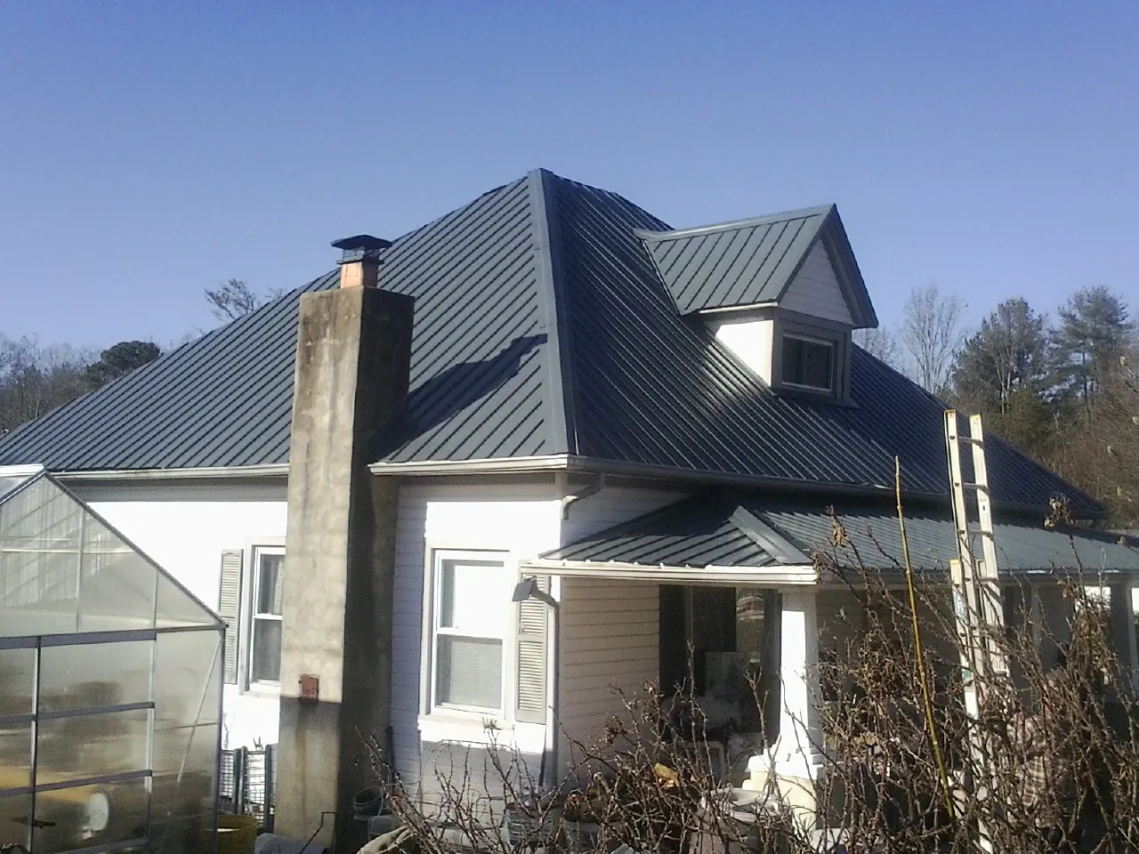Dark blue standing seam metal roof on a white farmhouse with dormer — Slate & Tile Roof Repair by Roofing Brothers in Lake Wales