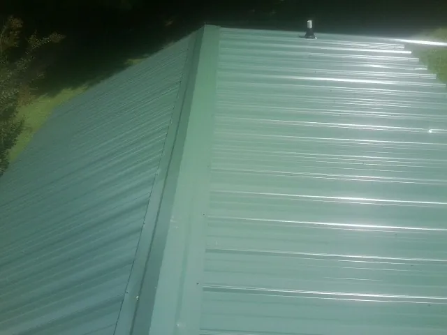 New green metal panels meeting at the ridge of a roof — Flat Roof Repair work by our crew in Lake Wales