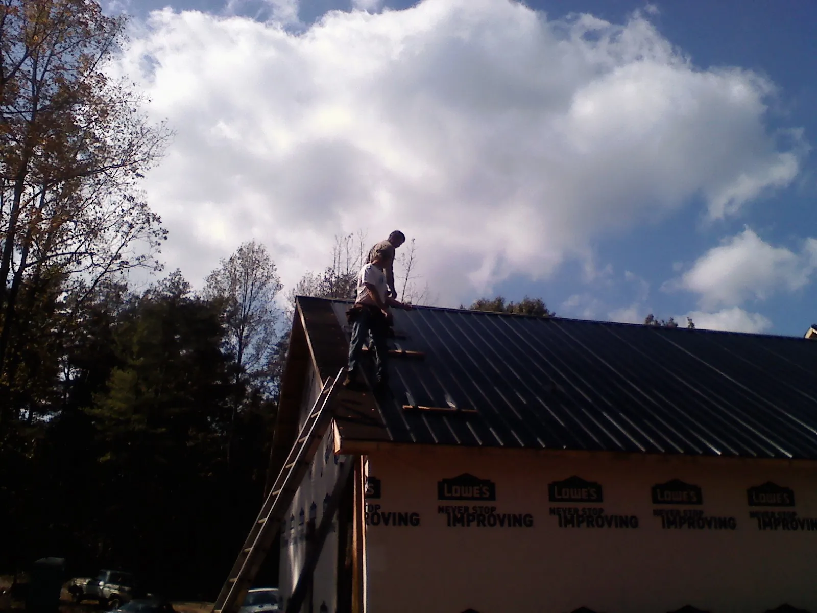 Roofer fastening dark metal panels high against a cloudy sky, from a Roof Inspection job in Lake Wales