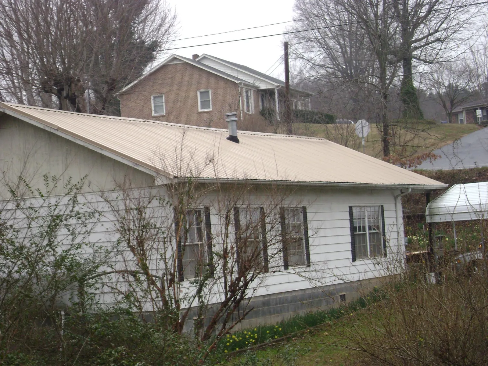 Tan metal roof on a white sided house set into a hillside — Commercial Roofing by Roofing Brothers in Lake Wales