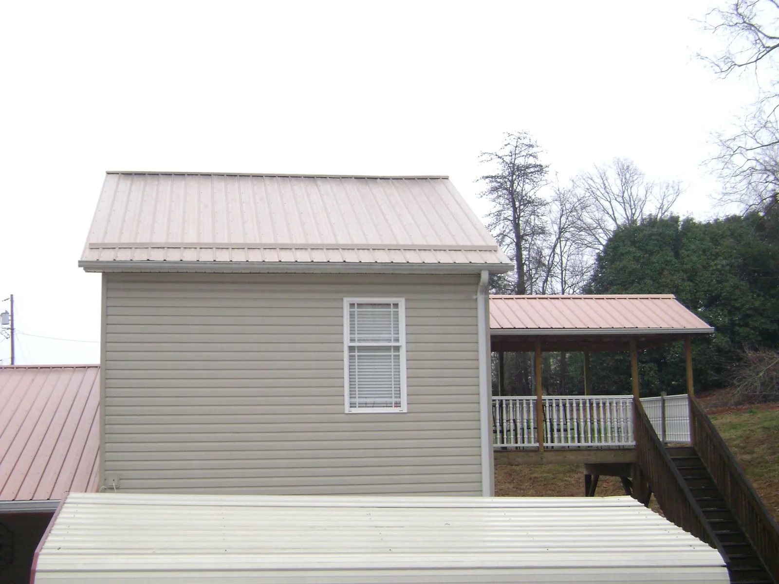 Tan metal roofs on a two story addition and attached porch, from a Roof Replacement job in Lake Wales